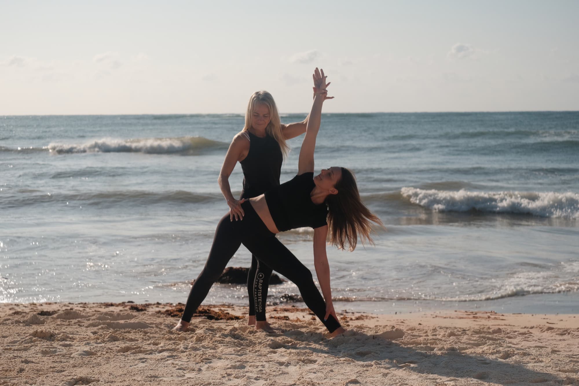 Gudrun teaching a yoga adjustment on the beach in Tulum